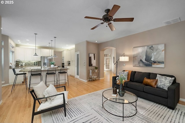 living room with arched walkways, light wood-type flooring, visible vents, and baseboards