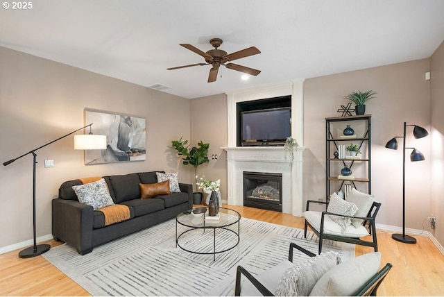 living area featuring ceiling fan, baseboards, wood finished floors, and a glass covered fireplace