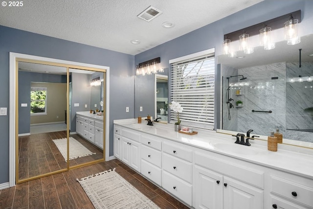 full bathroom with a sink, visible vents, wood tiled floor, double vanity, and walk in shower