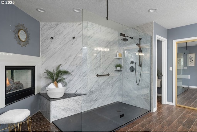 bathroom with wood tiled floor, a warm lit fireplace, a textured ceiling, and walk in shower