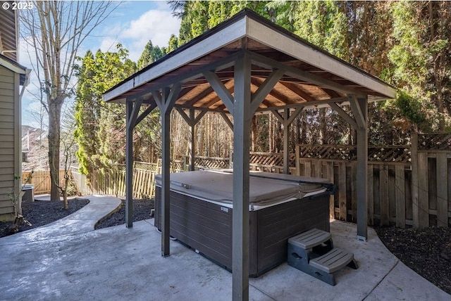 view of patio featuring a hot tub, fence, and a gazebo