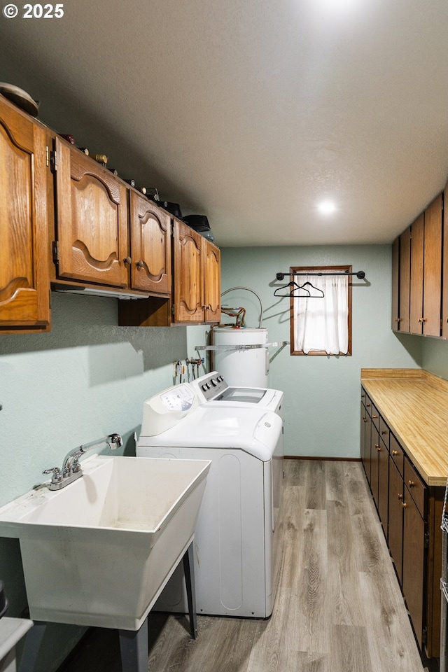 laundry room with sink, secured water heater, washer and clothes dryer, cabinets, and light wood-type flooring