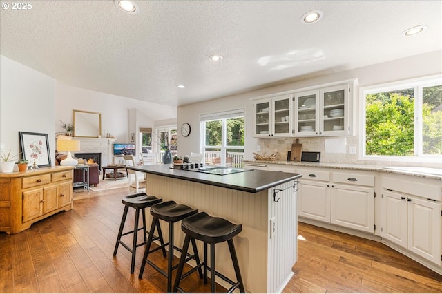 14940 SW Michael Ct, Sherwood, OR 97140 - kitchen with black electric cooktop, light wood-style floors, a breakfast bar area, a warm lit fireplace, and glass insert cabinets
