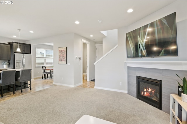 living area featuring recessed lighting, a tiled fireplace, light wood-style flooring, light carpet, and baseboards