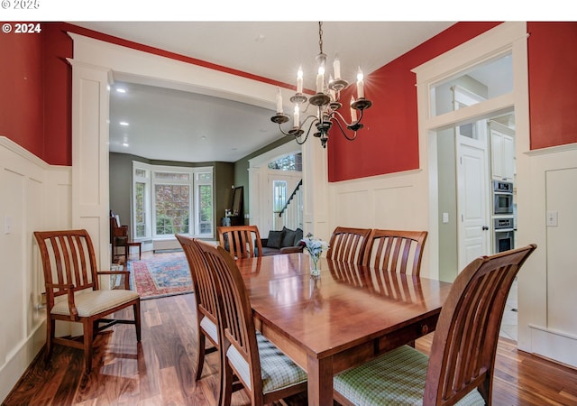 dining area with a notable chandelier, wood finished floors, stairs, and a decorative wall