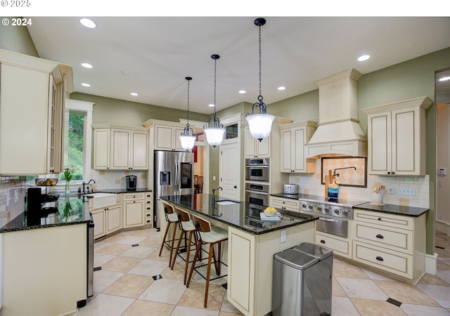 kitchen featuring cream cabinetry, custom exhaust hood, stainless steel appliances, a sink, and an island with sink