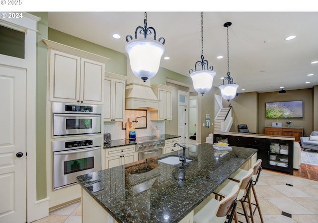 kitchen featuring tasteful backsplash, custom range hood, open floor plan, a sink, and a large island with sink