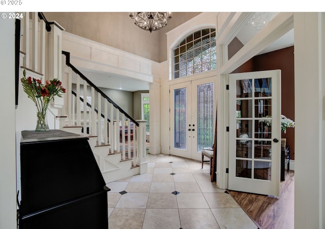 foyer entrance featuring light tile patterned floors, a towering ceiling, an inviting chandelier, stairs, and french doors