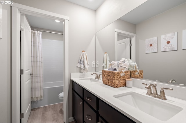 bathroom featuring double vanity, shower / tub combo, a sink, and wood finished floors