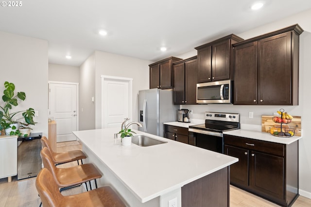 kitchen with appliances with stainless steel finishes, light countertops, a sink, and a center island with sink