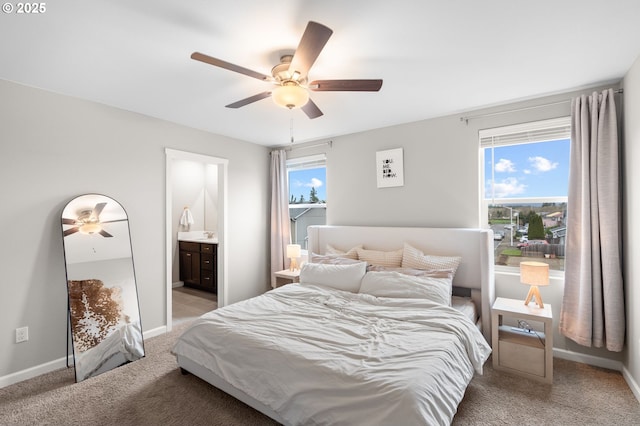 bedroom featuring ceiling fan, ensuite bath, light colored carpet, and baseboards