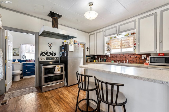 kitchen featuring appliances with stainless steel finishes, wood-type flooring, white cabinets, a kitchen bar, and open shelves