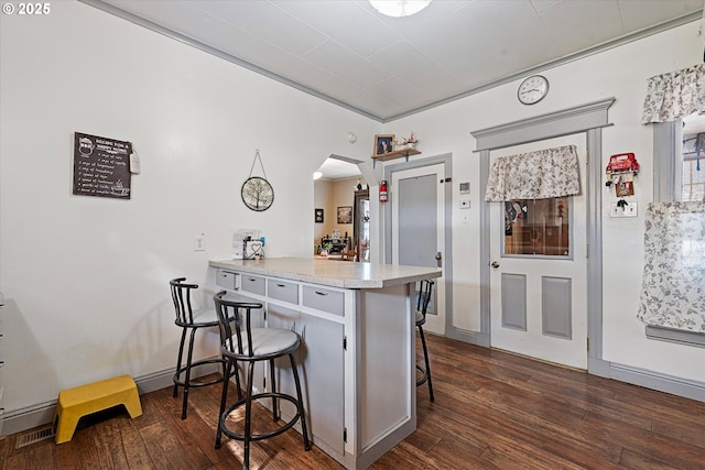 kitchen featuring a kitchen bar, dark wood-type flooring, arched walkways, light countertops, and a peninsula