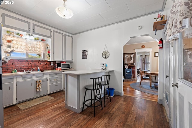 kitchen with stainless steel microwave, dark wood-style flooring, arched walkways, and light countertops