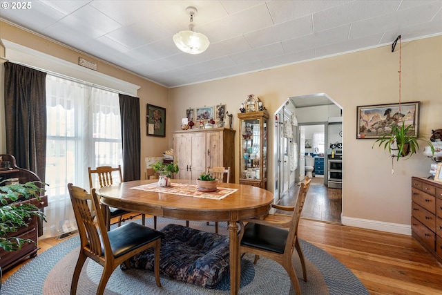 dining area featuring light wood-style floors, arched walkways, crown molding, and baseboards