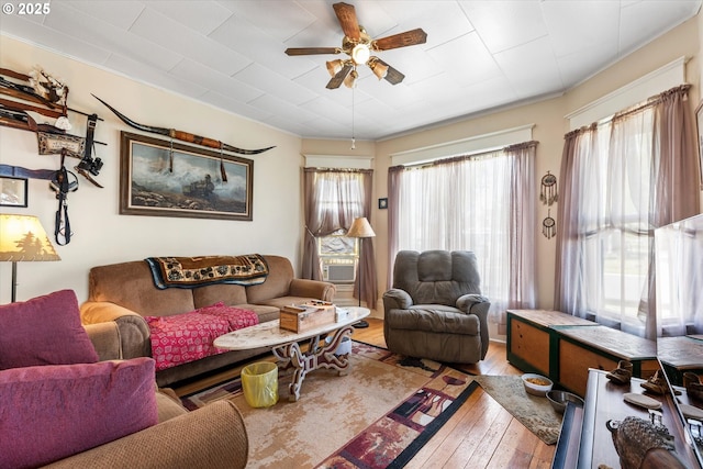 living area with wood-type flooring, a ceiling fan, and crown molding