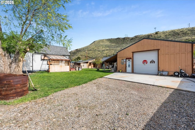 view of green lawn with driveway, a mountain view, an outdoor structure, and a garage