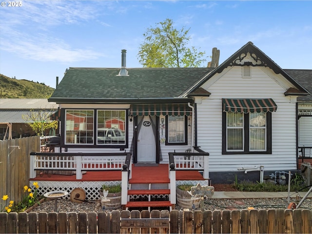 view of front of home featuring a porch, a fenced front yard, and roof with shingles
