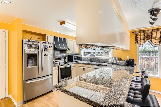 17180 NW Joscelyn St, Beaverton, OR 97006 - kitchen featuring appliances with stainless steel finishes, tile counters, wall chimney exhaust hood, a peninsula, and a sink