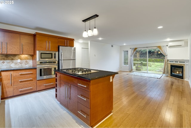 kitchen featuring a kitchen island, backsplash, hanging light fixtures, stainless steel appliances, and light wood-type flooring