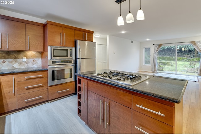 kitchen featuring appliances with stainless steel finishes, tasteful backsplash, dark stone countertops, hanging light fixtures, and a center island