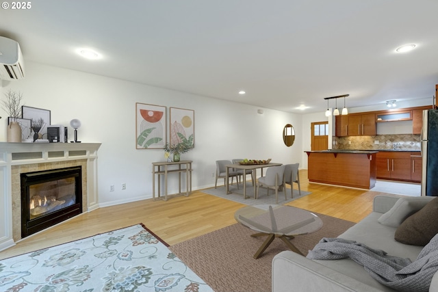 living room featuring a tiled fireplace, a wall mounted air conditioner, and light hardwood / wood-style floors