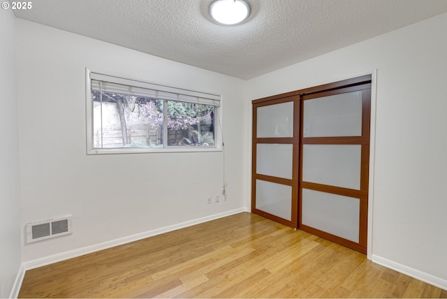 unfurnished bedroom featuring a closet, a textured ceiling, and light wood-type flooring