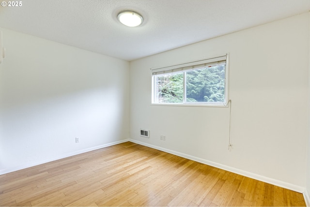 spare room with a textured ceiling and light hardwood / wood-style flooring