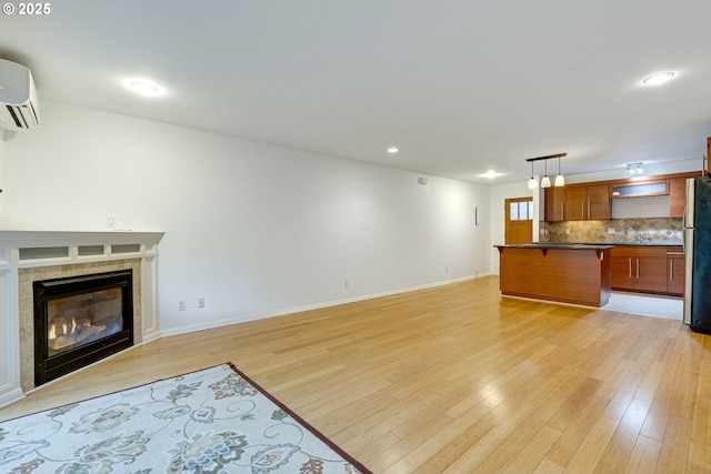 unfurnished living room featuring light hardwood / wood-style floors, an AC wall unit, and a tile fireplace