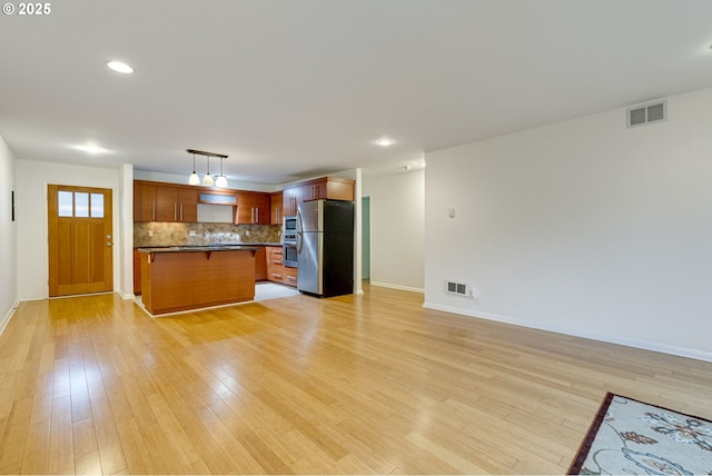 kitchen featuring appliances with stainless steel finishes, decorative light fixtures, decorative backsplash, and light wood-type flooring