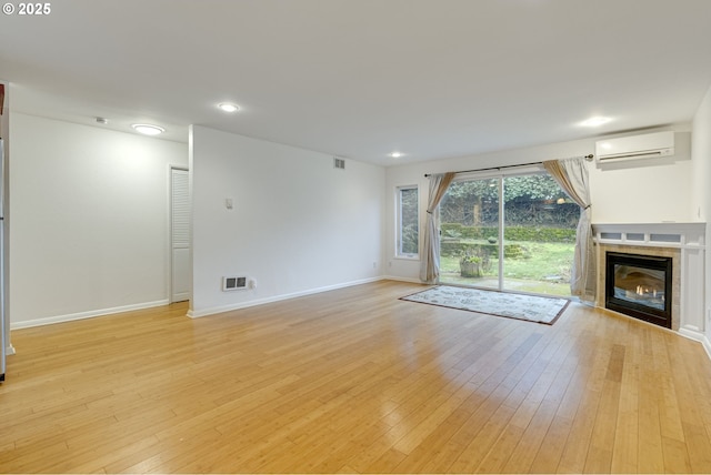 unfurnished living room with a wall mounted air conditioner, a fireplace, and light hardwood / wood-style floors