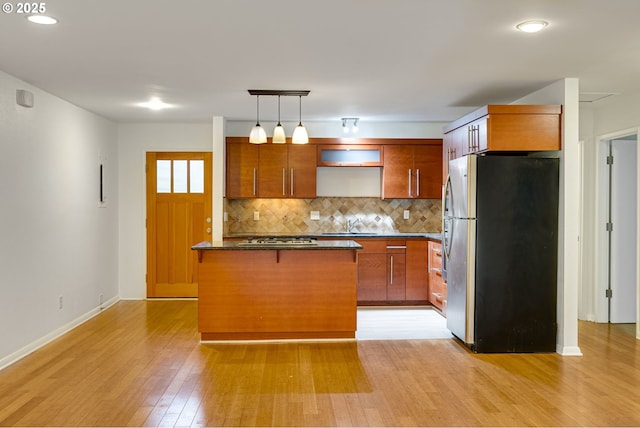 kitchen featuring pendant lighting, backsplash, stainless steel appliances, a center island, and light wood-type flooring