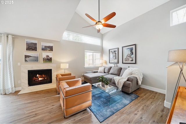 living area featuring light wood finished floors, high vaulted ceiling, baseboards, and a high end fireplace