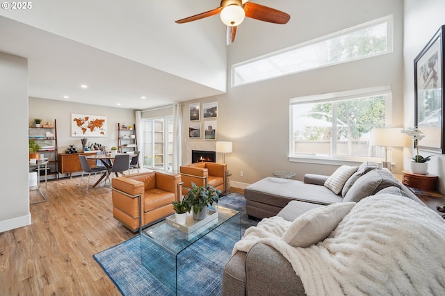 living room featuring recessed lighting, light wood-style floors, baseboards, and a warm lit fireplace