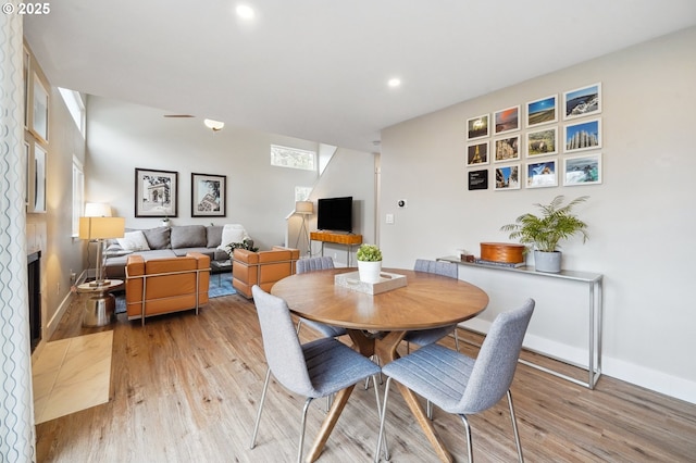 dining area with recessed lighting, baseboards, a large fireplace, and light wood-style floors