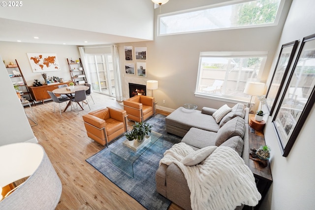 living area featuring wood finished floors, baseboards, recessed lighting, a lit fireplace, and a towering ceiling