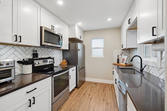 kitchen with light wood-type flooring, a sink, dark countertops, appliances with stainless steel finishes, and white cabinets