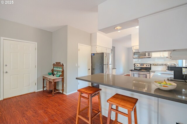 17474 SW Sarala St, Beaverton, OR 97007 - kitchen featuring appliances with stainless steel finishes, dark wood-type flooring, a peninsula, white cabinetry, and dark countertops