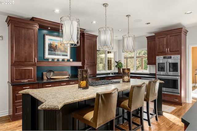 kitchen featuring light stone countertops, a kitchen island, light wood-style flooring, appliances with stainless steel finishes, and decorative light fixtures