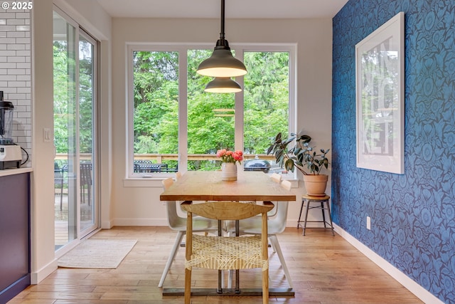 dining area with wallpapered walls, light wood-type flooring, baseboards, and a wood stove