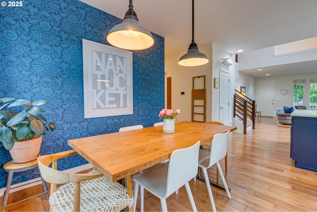 dining space featuring wallpapered walls, light wood finished floors, stairway, an accent wall, and baseboards