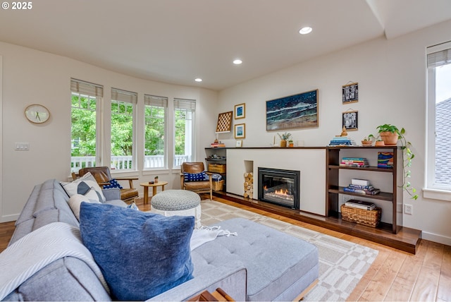 living room featuring light wood-style floors, a glass covered fireplace, recessed lighting, and baseboards