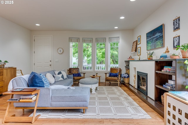 living room with recessed lighting, a glass covered fireplace, and light wood-type flooring