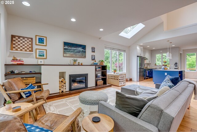 living room with light wood-style flooring, a skylight, a glass covered fireplace, recessed lighting, and lofted ceiling