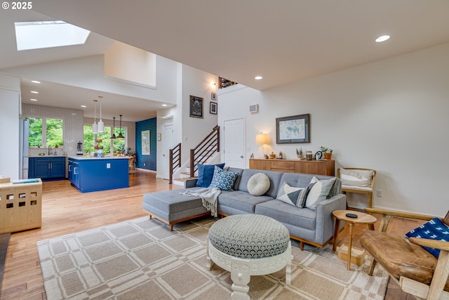 living area featuring stairway, recessed lighting, light wood finished floors, a skylight, and high vaulted ceiling
