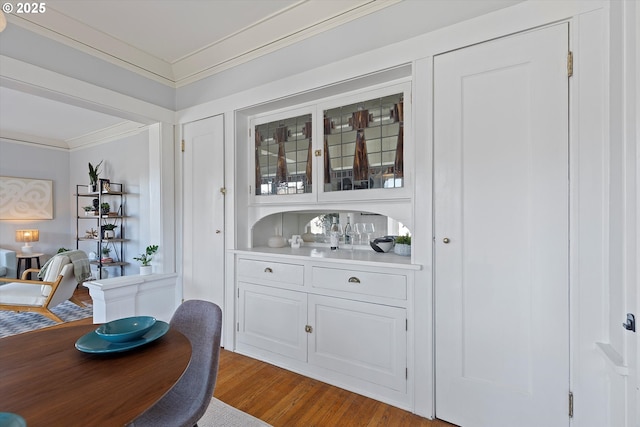 bar with hardwood / wood-style flooring, ornamental molding, and white cabinets