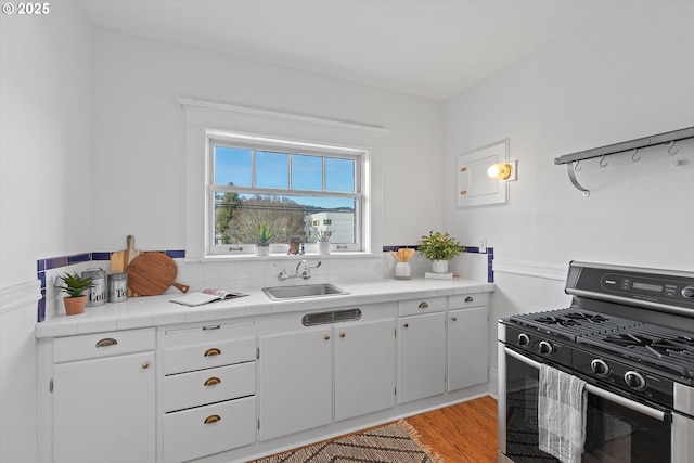 kitchen featuring black range with gas stovetop, tile counters, light hardwood / wood-style floors, and sink