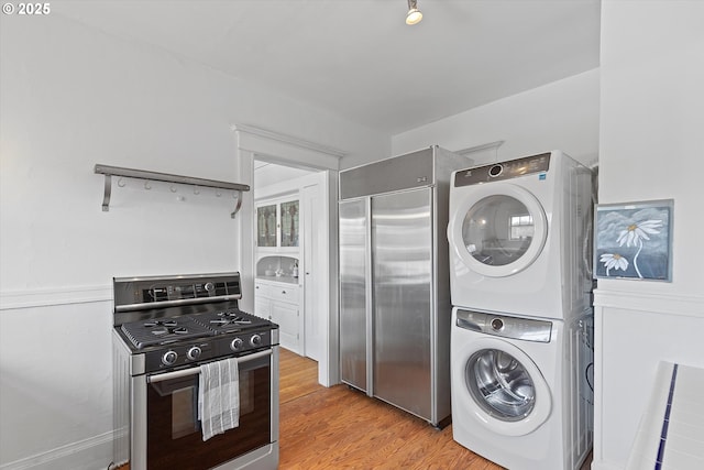 kitchen featuring built in refrigerator, gas range, light hardwood / wood-style floors, and stacked washer / dryer