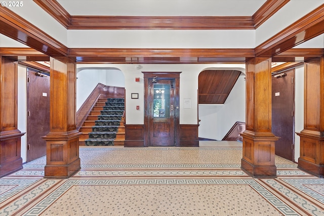 foyer with crown molding, decorative columns, and wood walls