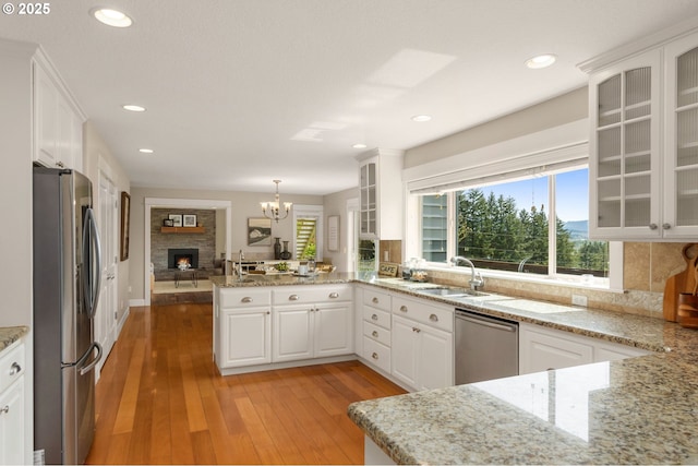 kitchen featuring a stone fireplace, appliances with stainless steel finishes, a sink, a peninsula, and white cabinetry
